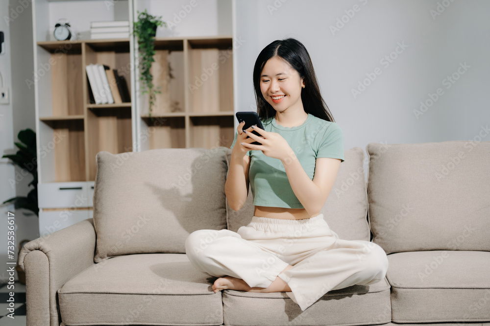 Young asian woman using smartphone and tablet while seated on couch at home. Young asian woman using smartphone and tablet while seated on couch at home.