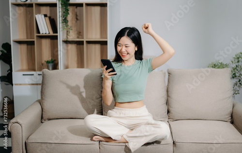 Young asian woman using smartphone and tablet while seated on couch at home.