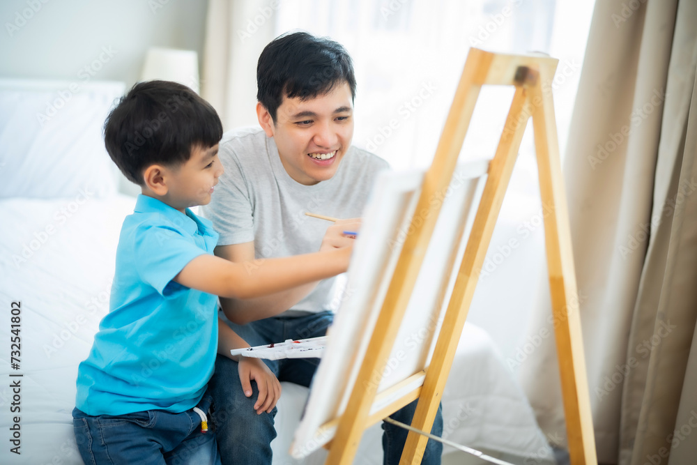 Young Asian Child and dad painting together on canvas and stand with smile of fun and happiness at home, relationship, activity with father and boy. Young Asian Child and dad painting together on canvas and stand with smile of fun and happiness at home, relationship, activity with father and boy.
