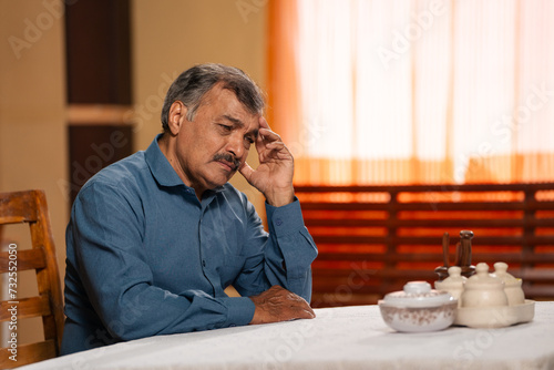 Thoughtful worried senior man at home on dinging table - concept of mental wellness, contemplation and concern or family problems.