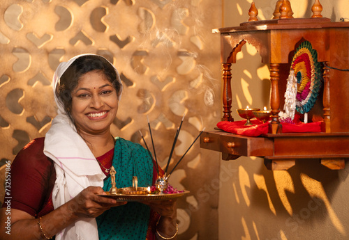 Devotional Indian woman with Pooja thali plate offering aarthi to god by looking camera at home - Concept of Hinduism  spirituality and morning rituals or custom