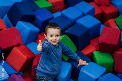 Little boy, happy smiling child lying down playing with soft colored cubes in playroom, showing thumbs up, like. Photography, portrait, childhood concept.