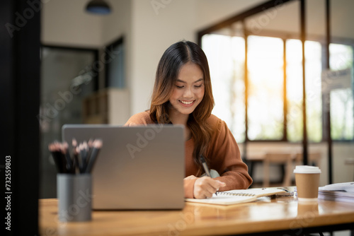 Cheerful young woman in casual attire focusing on a laptop screen, working from a modern office.