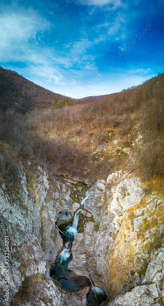 Panoramic view of Blue Sini vir waterfall at Medven, near Kotel, Bulgaria. Spring green view of a beautiful waterfall among cliffs. Emerald lake and blue sky. Panorama - Image