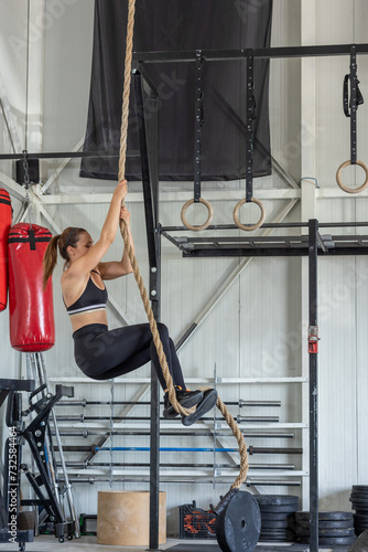 A young woman using her arms and feet to climb a rope in a gym