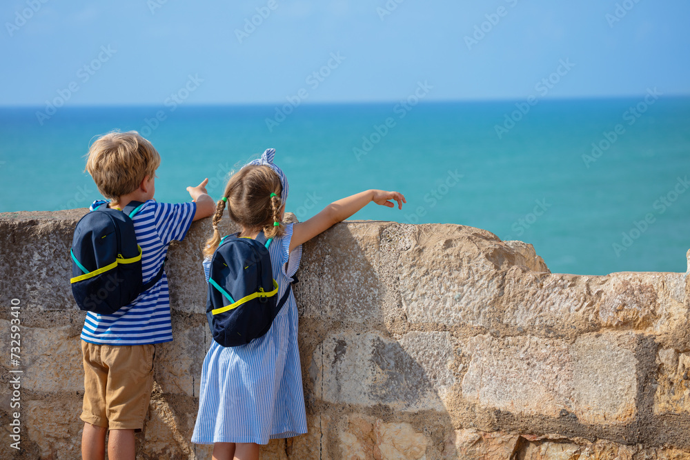 Young tourists boy and girl with little backpacks point at sea Young tourists boy and girl with little backpacks point at sea