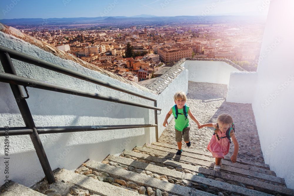 Two little travelers climb up hill in Granada town, Spain