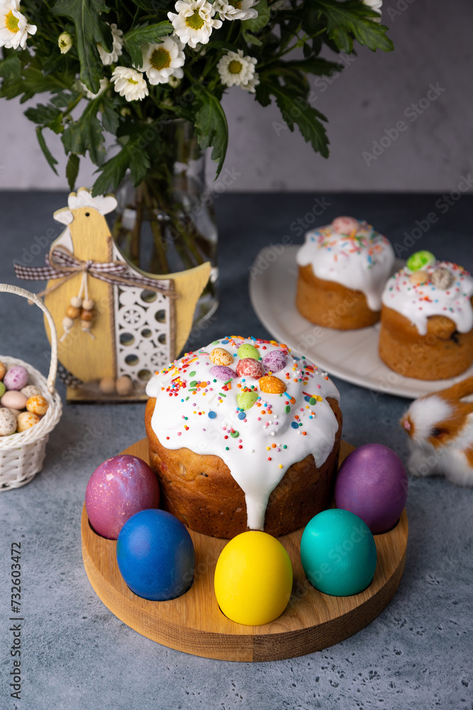 Easter kulich with candied fruits in white glaze with colorful sprinkles and painted eggs. Traditional Easter pastry. Easter holiday. Close-up, selective focus.