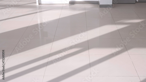 Sunlight and long shadow pattern of glass wall frame on surface of gray ceramic tile floor inside of living room, high angle view with copy space
