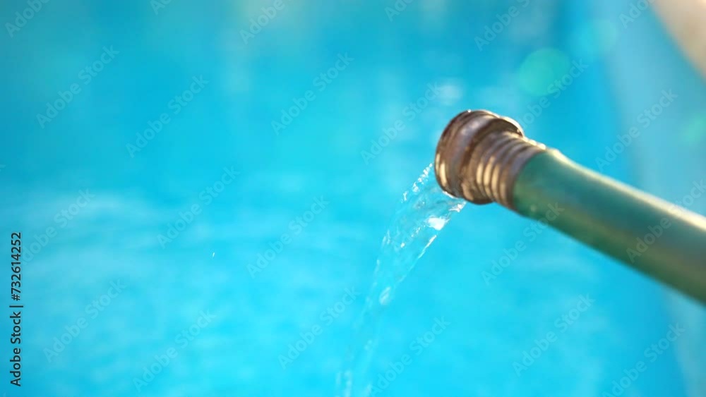 Close up stream of water flowing from a green hose and filling a clean blue swimming pool in the backyard. Weekly pool maintenance and cleaning Close up stream of water flowing from a green hose and filling a clean blue swimming pool in the backyard. Weekly pool maintenance and cleaning