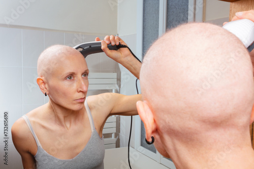 Woman without hair guides slowly electric shaver over her head