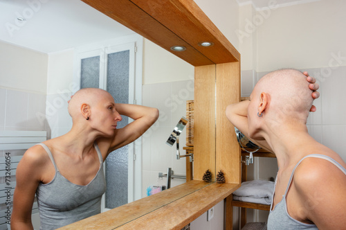 Woman with no hair contemplates her reflection in a mirror