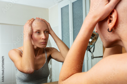 Ill woman with no hair examines her reflection attentively