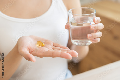Dietary supplement, asian young woman, girl hand holding medical pill capsule, take or eat vitamin C, D for treatment for skin, hair and nail strengthen with glass of pure water at home, healthcare. © KMPZZZ