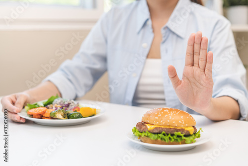 Diet concept, asian young woman hand reject eat burger, hamburger on plate, push out or deny to eat fast, junk food choose green vegetable salad, girl eat low fat for good healthy, getting weight loss