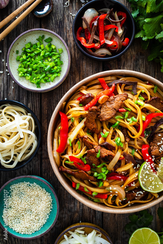 Asian style stir fried vegetables, roast beef and chow mein noodles to go in food box on wooden table 