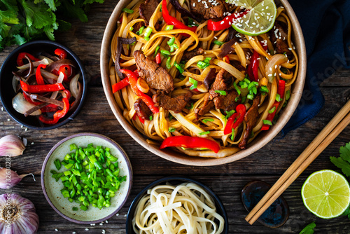 Asian style stir fried vegetables, roast beef and chow mein noodles  to go  in food box on wooden table
 photo