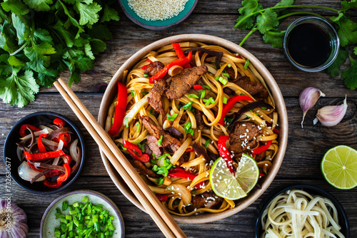 Asian style stir fried vegetables, roast beef and chow mein noodles  to go  in food box on wooden table
 photo