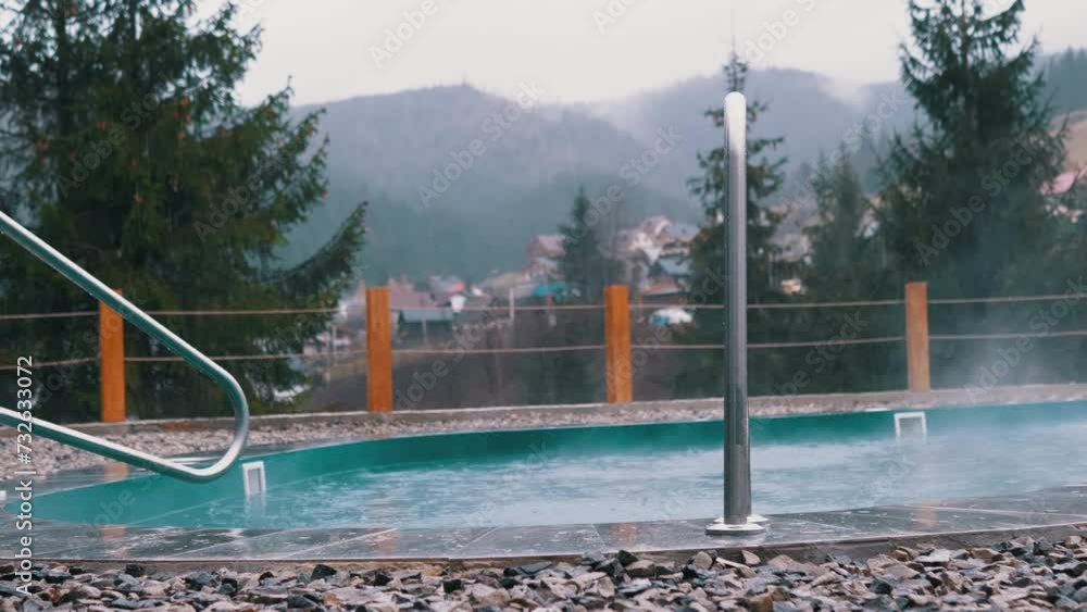 Empty Swimming Pool against the Backdrop of Rain with a View of the Mountains. Raindrops falling into an empty hot tub with blue hot water from thermal springs. Outdoors. Evaporation. Spa hotel. Empty Swimming Pool against the Backdrop of Rain with a View of the Mountains. Raindrops falling into an empty hot tub with blue hot water from thermal springs. Outdoors. Evaporation. Spa hotel.