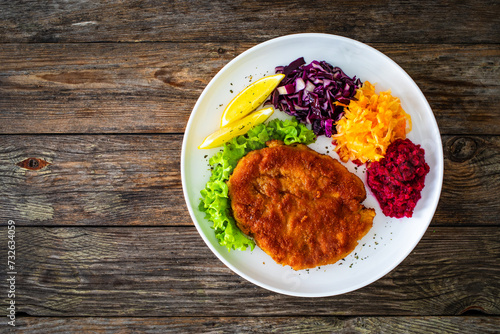 Crispy breaded fried pork chop with grated beetroots, red cabbage and sauerkraut on wooden table
 photo
