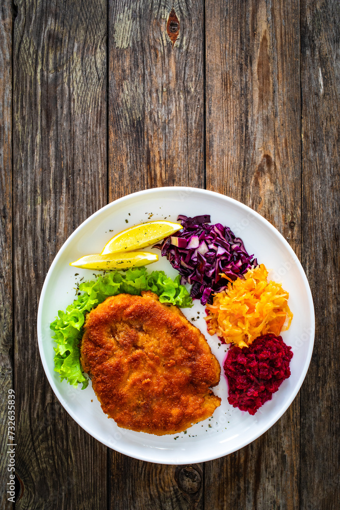 Crispy breaded fried pork chop with grated beetroots, red cabbage and sauerkraut on wooden table
Crispy breaded fried pork chop with grated beetroots, red cabbage and sauerkraut on wooden table