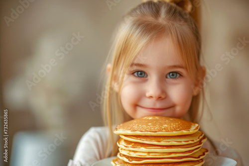 Beautiful little smiling girl holding a stack of sweet pancakes on a plate in front of the camera 