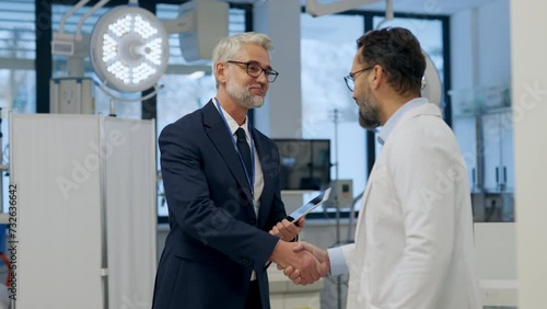 Pharmaceutical sales representative presenting new medication to doctor in medical building, shaking hands.
