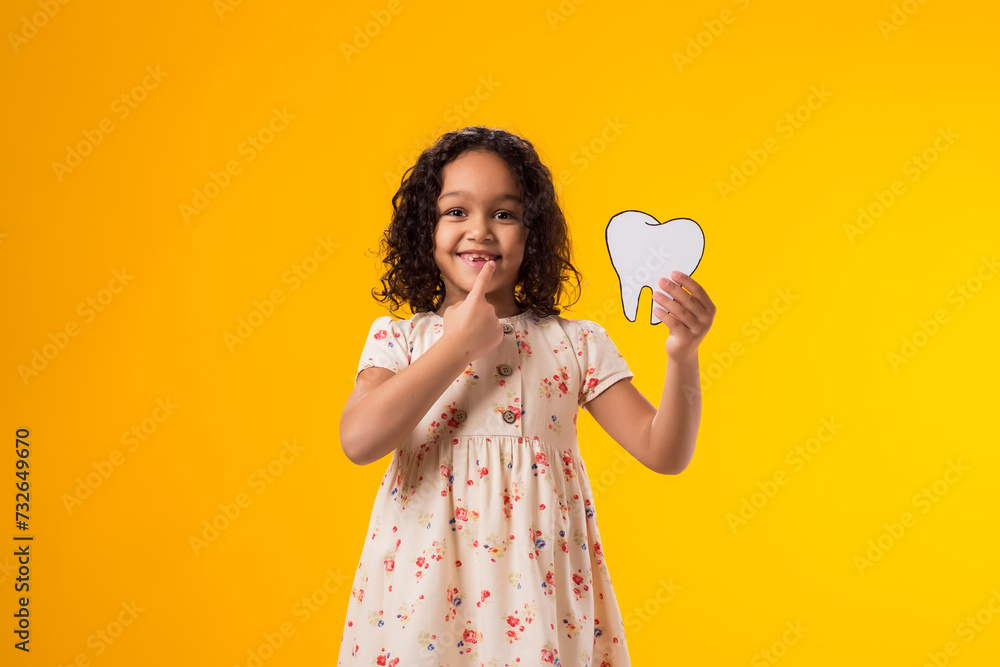 Child girl holding papercraft tooth and touching her tooth. Dental health concept Child girl holding papercraft tooth and touching her tooth. Dental health concept