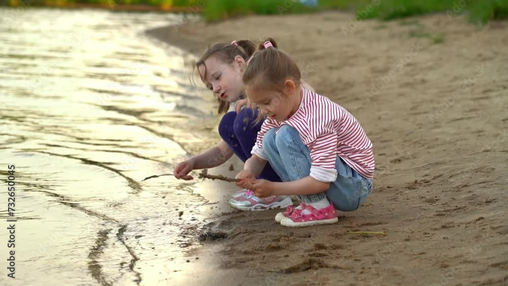Happy little girls play with sand and water on river shore in summer park. Active childrens leisure games. Outdoors Happy little girls play with sand and water on river shore in summer park. Active childrens leisure games. Outdoors