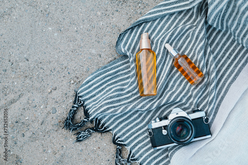 A peshtemal cotton towel with sunscreen skin care products and film camera on the sand of a wild beach photo