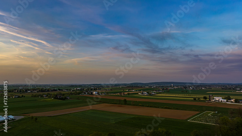 Expansive View Of A Rural Landscape At Twilight With Patchwork Fields, Sparse Buildings, And A Softly Colored Sky.