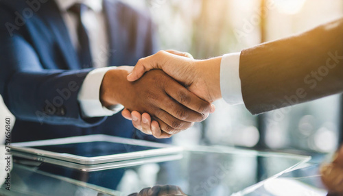 businesspeople shake hands over a sleek glass desk