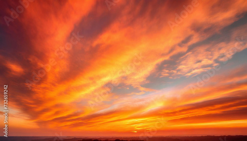 Beautiful sunset sky above the fluffy clouds illuminated in vibrant orange hues. Natural summer cloudscape
