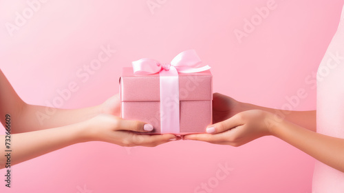 Hands presenting a pink gift box with a satin ribbon on a matching pastel pink background. © Александр Марченко