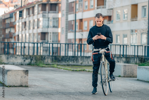 urban young man with mobile phone on top of the bicycle in the street