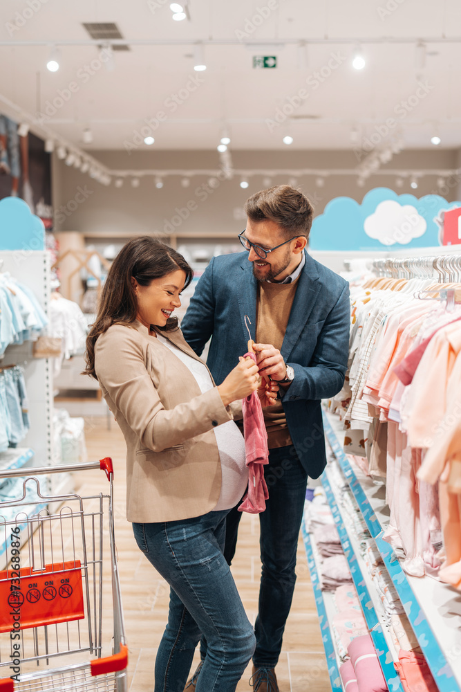 Attractive middle age couple enjoying in buying clothes and appliances for their new baby. Heterosexual couple in baby shop or store. Expecting baby concept.