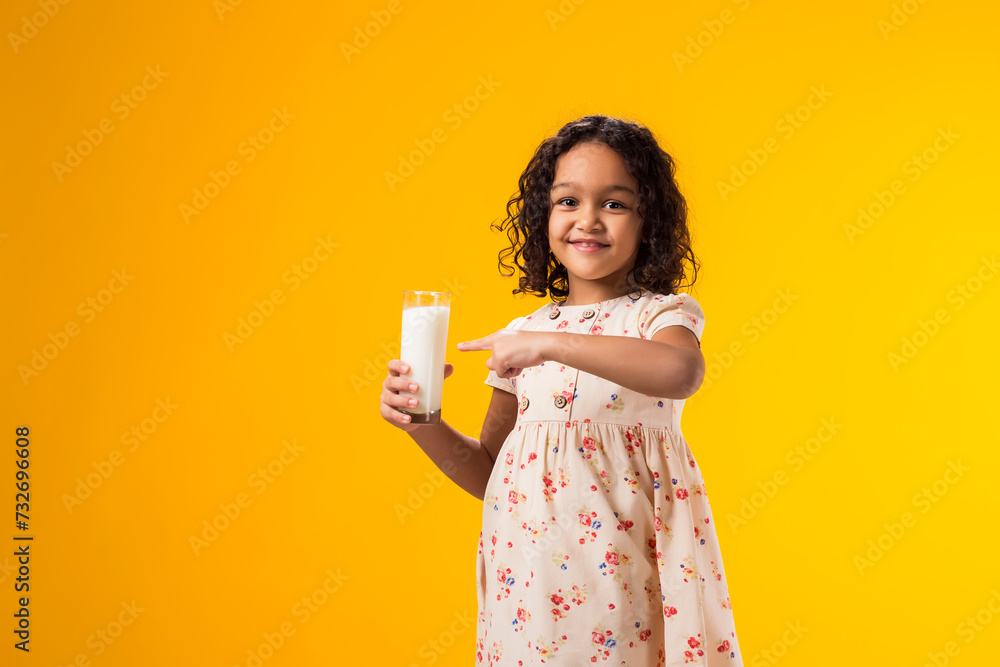 Smiling child girl holding glass of milk and pointing finger at it. Nutrition and health concept Smiling child girl holding glass of milk and pointing finger at it. Nutrition and health concept