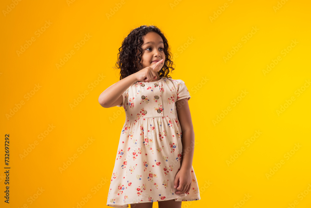 Smiling child girl pointing to an empty place on yellow background. Advertisement concept Smiling child girl pointing to an empty place on yellow background. Advertisement concept