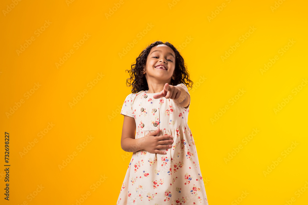 Kid girl mocking and teasing at someone showing finger at camera and holding stomach over yellow background. Bulling concept Kid girl mocking and teasing at someone showing finger at camera and holding stomach over yellow background. Bulling concept
