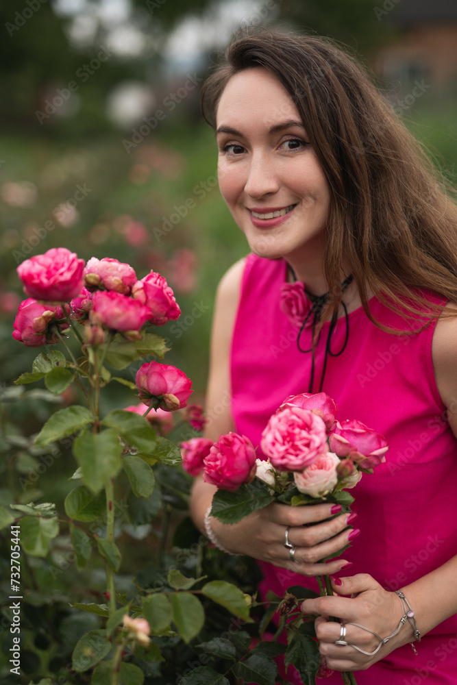 a beautiful girl in a pink dress is picking red roses in the garden