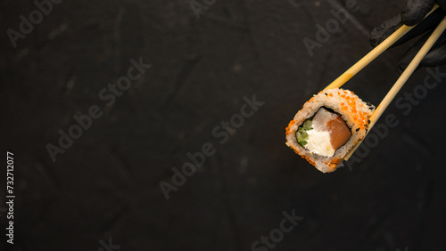 Sushi rolls on a dark background. The hand holds the roll. Sushi sticks