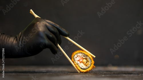 Sushi rolls on a dark background. The hand holds the roll. Sushi sticks
