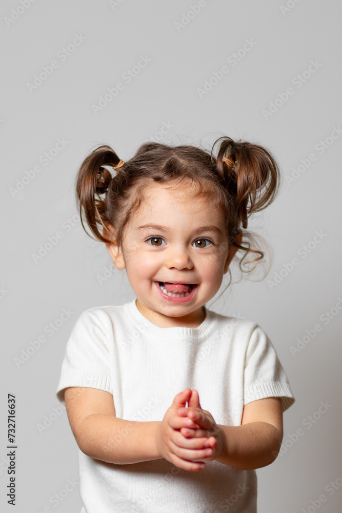 Cute caucasian brunette toddler girl with two tails in white dress excited smiling happiely on white background Cute caucasian brunette toddler girl with two tails in white dress excited smiling happiely on white background