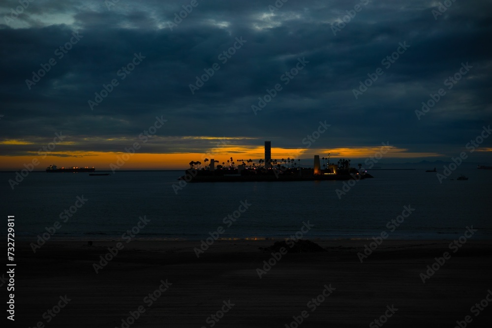 Naklejka premium Silhouette of an island illuminated by the setting sun against a tranquil, reflective ocean