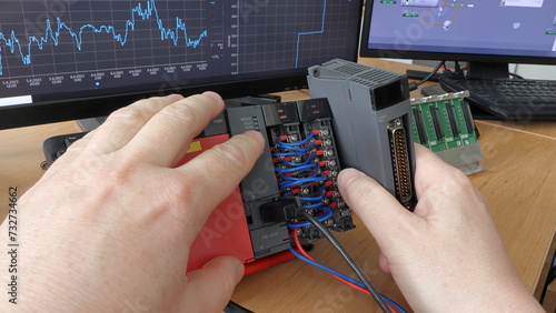 An electrical engineer adds a new IO card to a modular PLC automaton. Programmable logic controller. Trends of measured quantities in the background. Production automation. Automatic control system.
