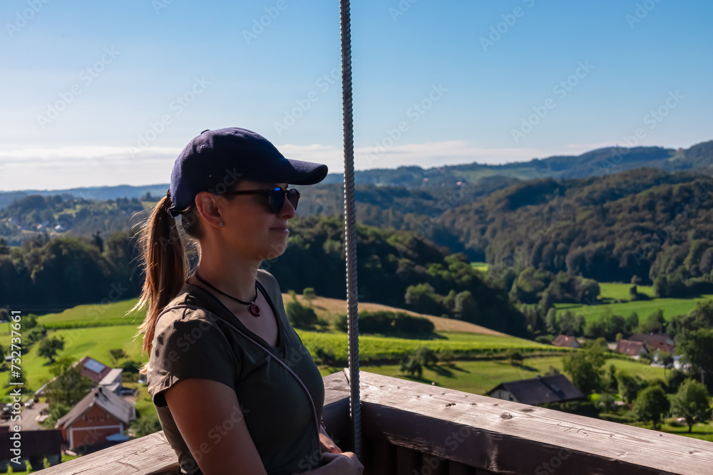 Naklejka premium Tourist woman with scenic view from Weinleiten water tower in Ehrenhausen an der Weinstrasse, Leibnitz, South Styria, Austria. Wine plantations and vineyards over lush green hills. Styrian Tuscany