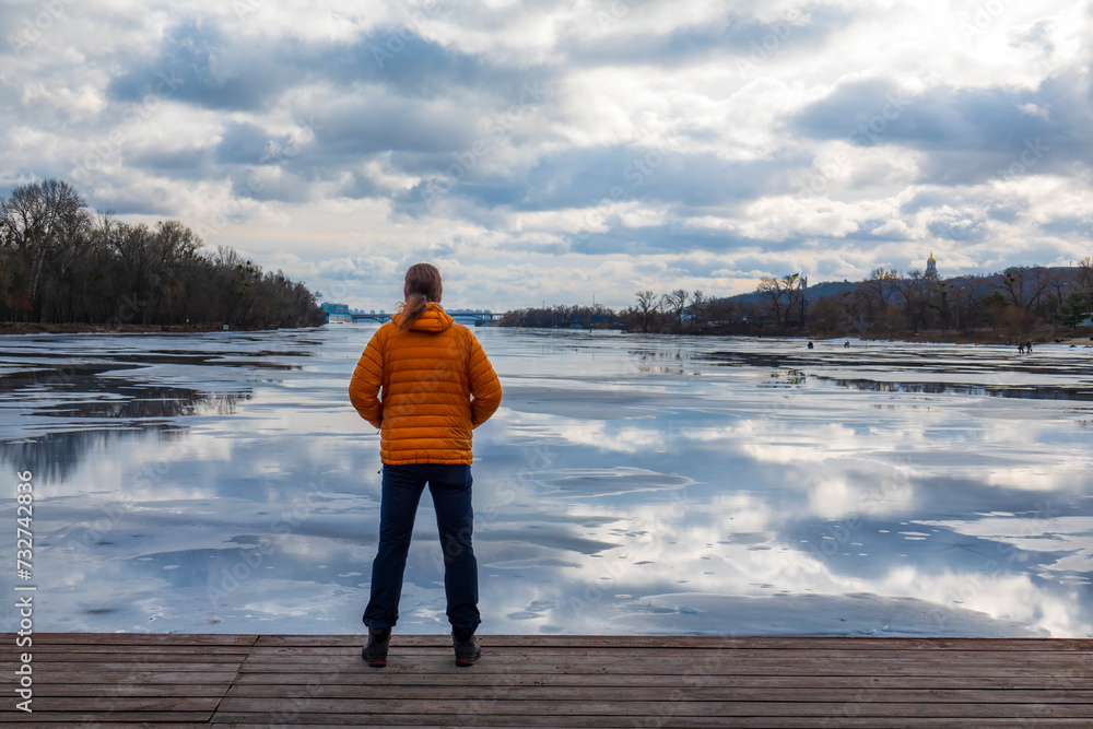 Lonely man in orange down jacket standing on a wooden pier