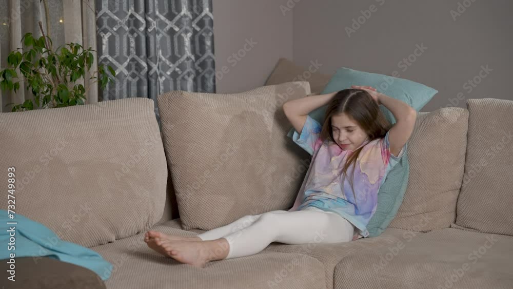 Smiling cute relaxed girl lying on sofa, enjoying rest. Happy positive kid resting on cozy couch, raising arms, stretching muscles, reposing indoors, watching tv at home Smiling cute relaxed girl lying on sofa, enjoying rest. Happy positive kid resting on cozy couch, raising arms, stretching muscles, reposing indoors, watching tv at home