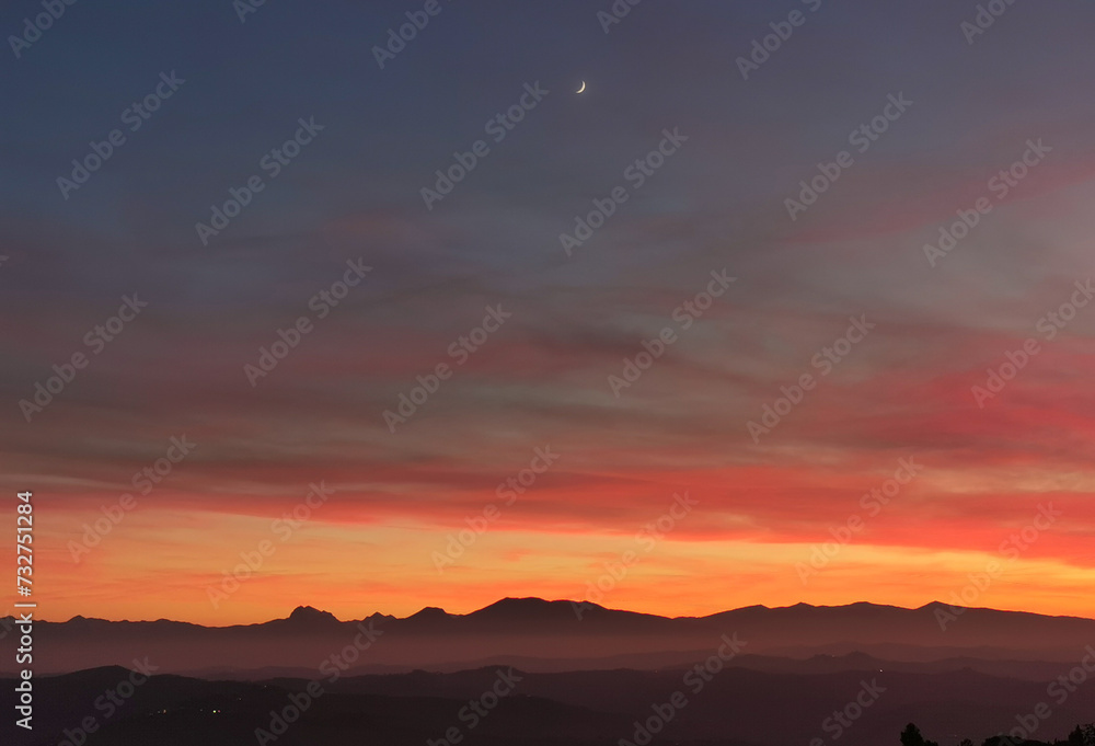 Obraz premium La Luna al tramonto nel cielo arancione sopra le montagne