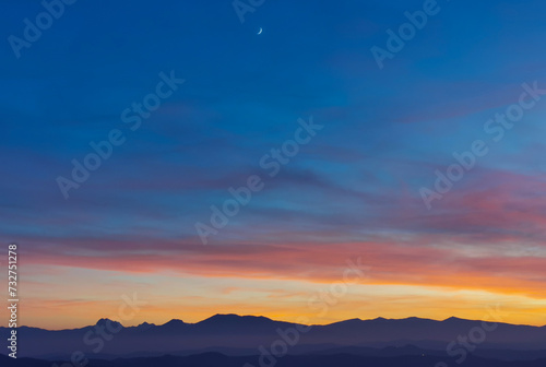 Tramonto blu e arancio con luna nel cielo sopra le valli e le montagne photo